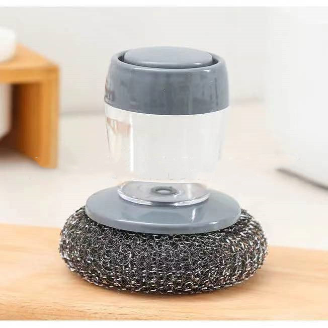 Cleaning brush with gray handle and metal scrubber on a wooden surface