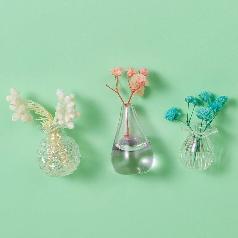 Three small glass vases with floral arrangements on a light green background