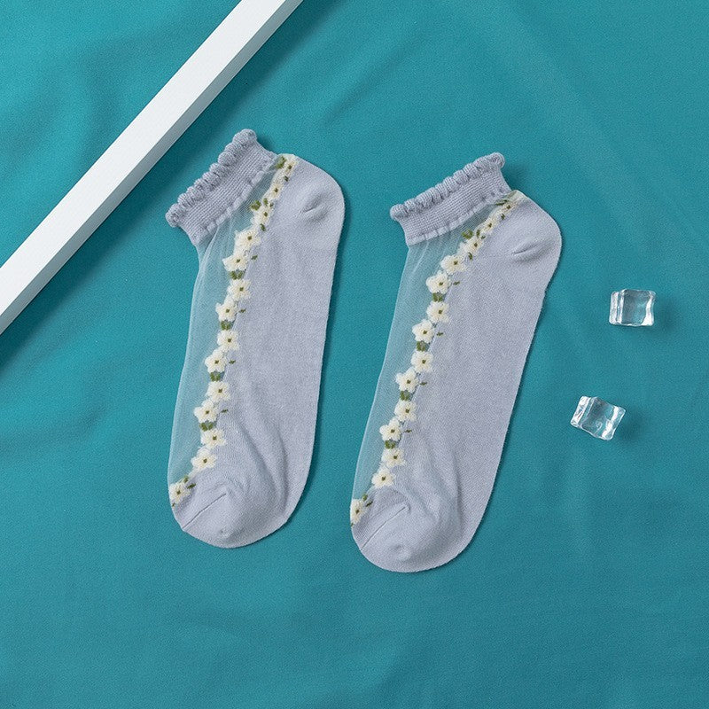 A pair of women's boat socks with a floral design in purple and white colors, worn with a pair of flat shoes.