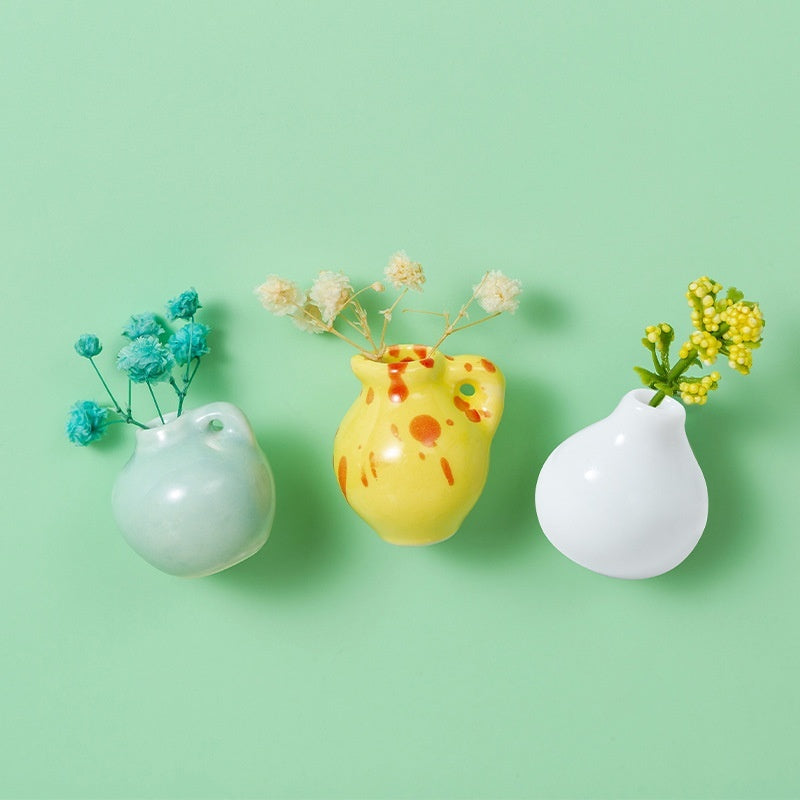Three small decorative vases with flowers on a light green background
