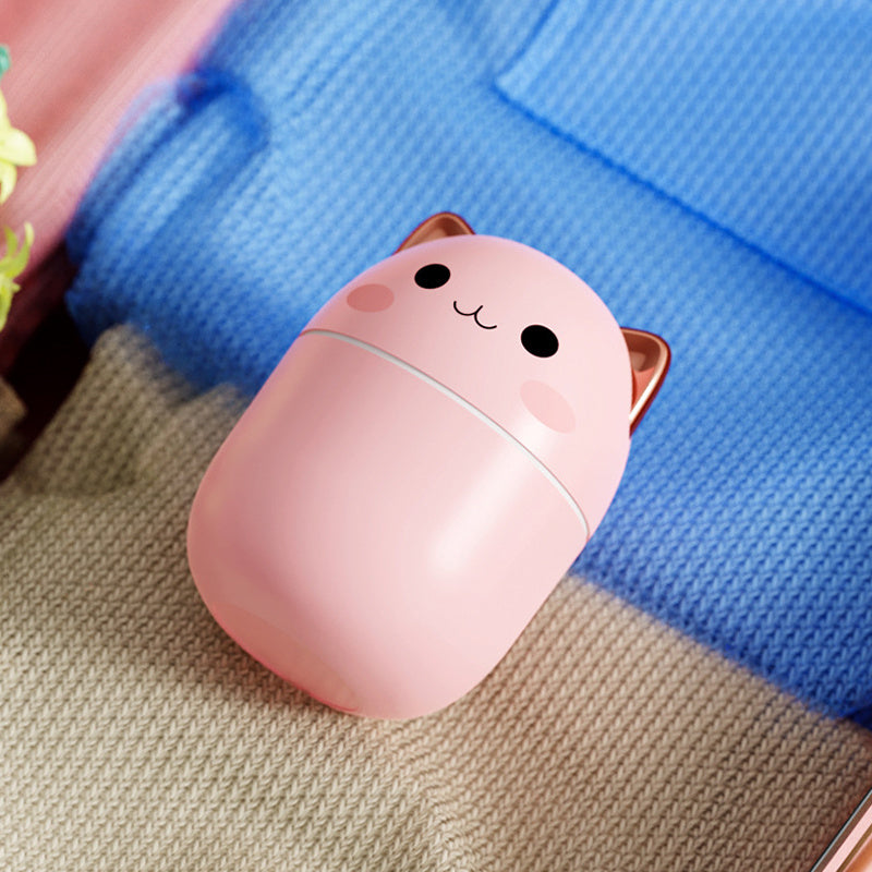 Pink cat-shaped compact mirror on a textured surface with a blue fabric background