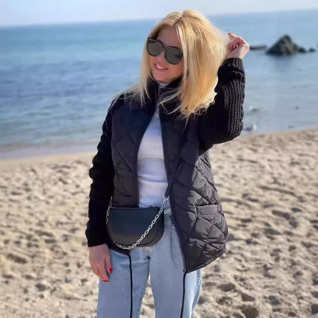 Woman on a beach wearing sunglasses and a black puffer vest with a white top and light blue jeans.