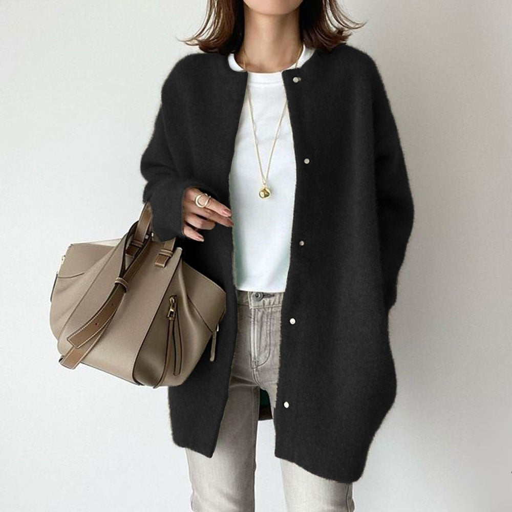 Person wearing a black cardigan holding a beige handbag on a plain background