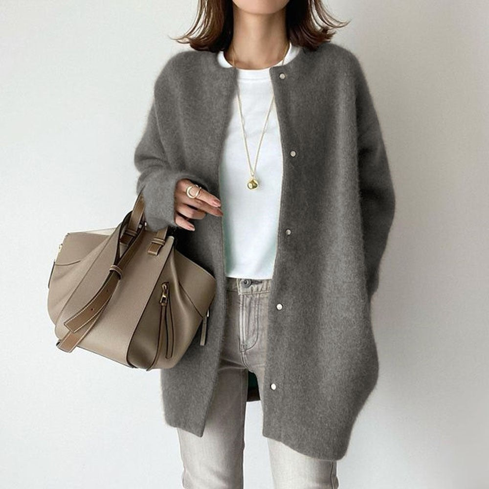 Person wearing a gray cardigan holding a beige handbag on a plain background