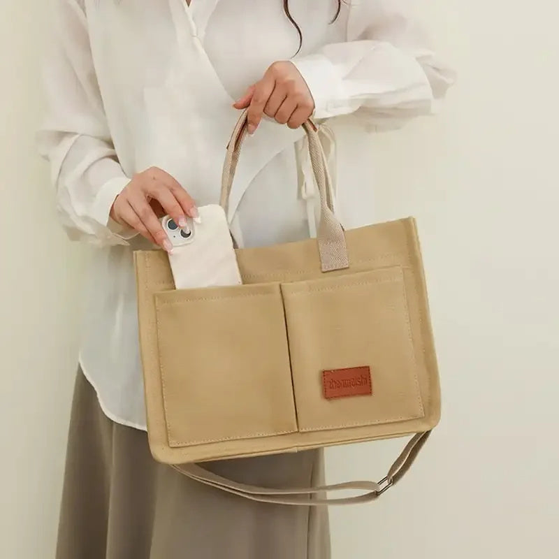 Person holding a beige tote bag with a visible brand label against a plain background