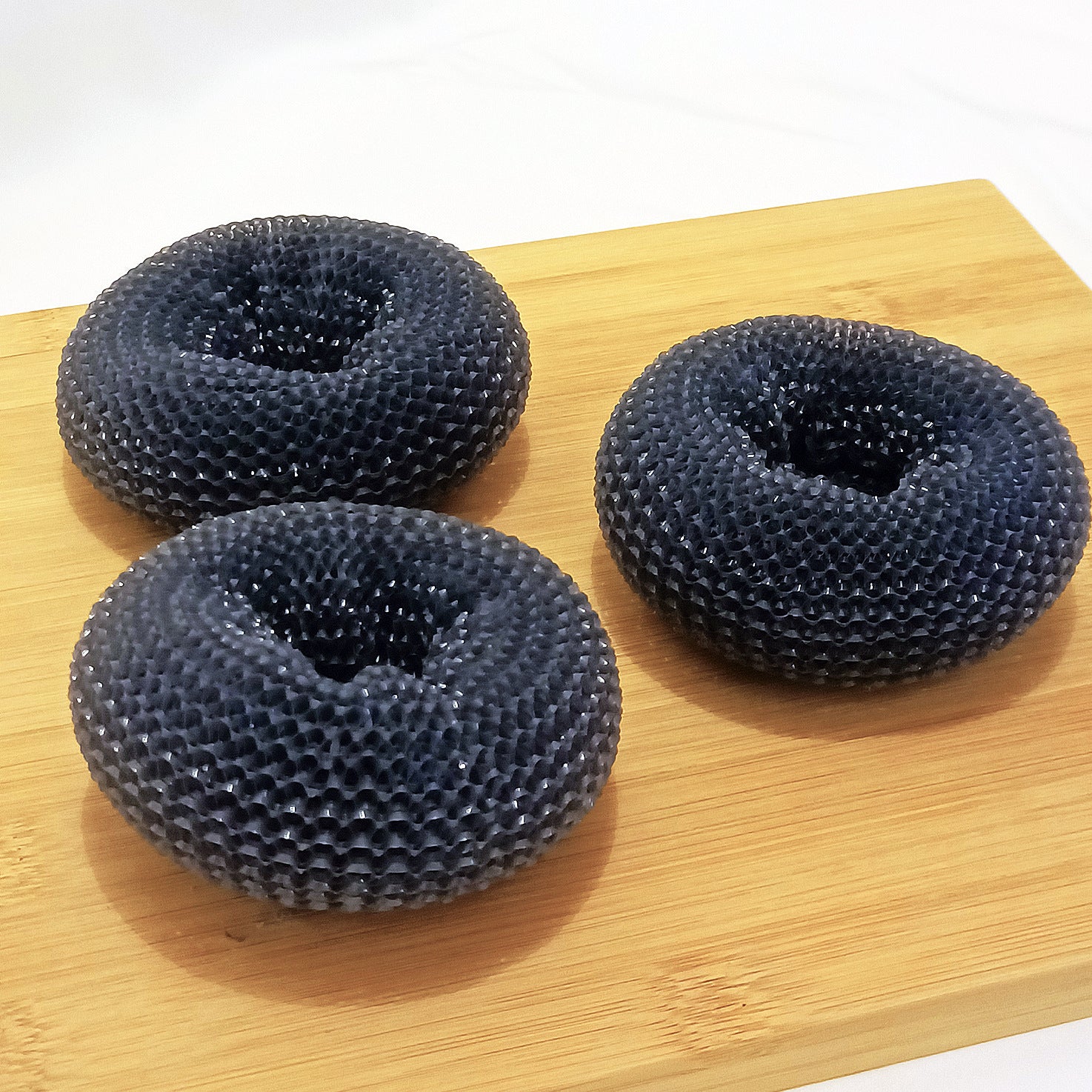 Three black honeycomb donut-shaped objects on a wooden board