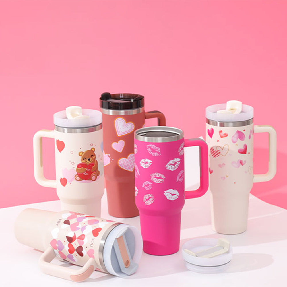 A collection of insulated tumblers with handles and straws, in various colors including white, pink, and red, adorned with heart patterns and other designs, intended for beverage insulation.